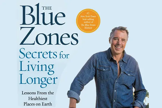 dan buettner parado em frente a uma capa de livro
